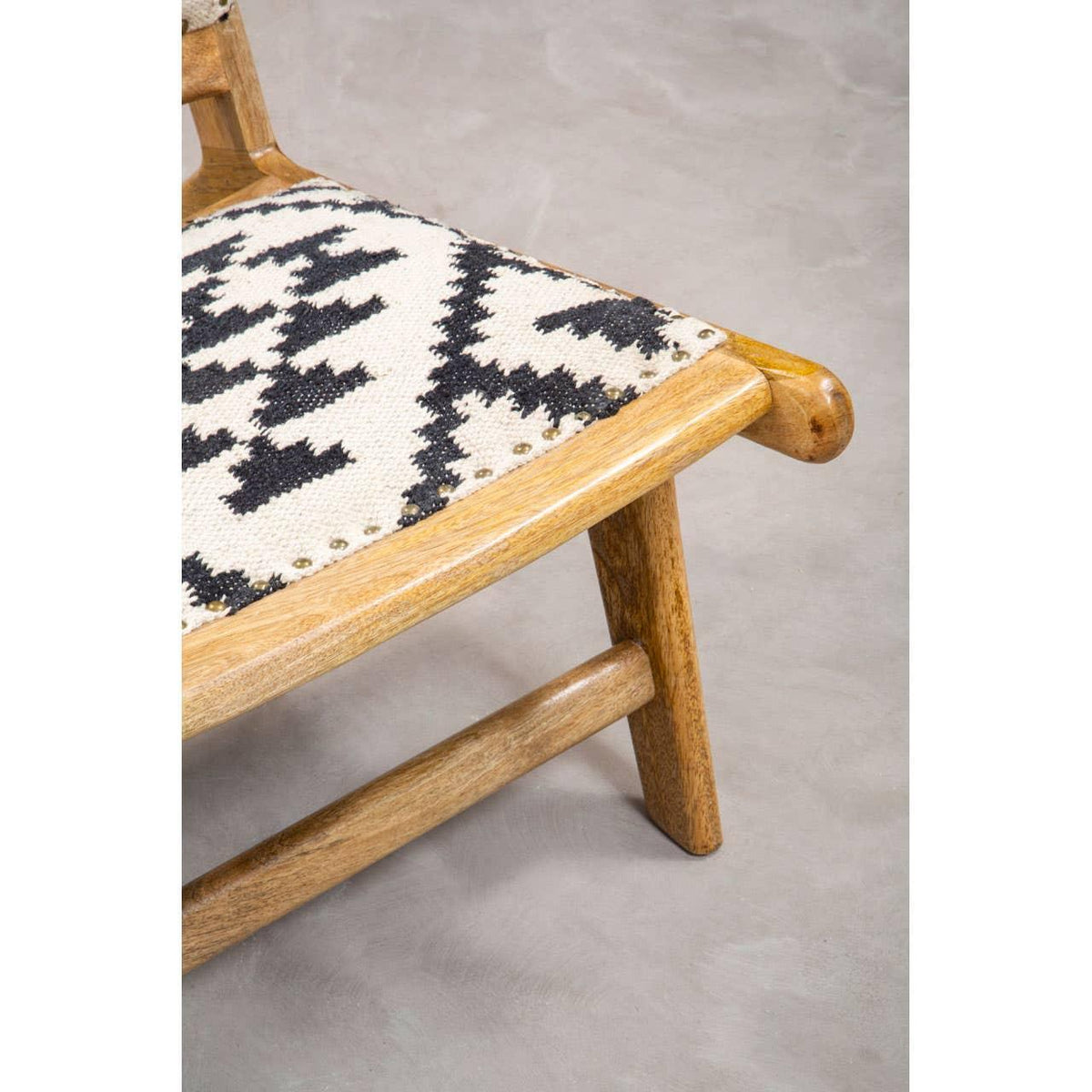 Closeup of wooden chair with black and white patterned fabric seat on grey floor