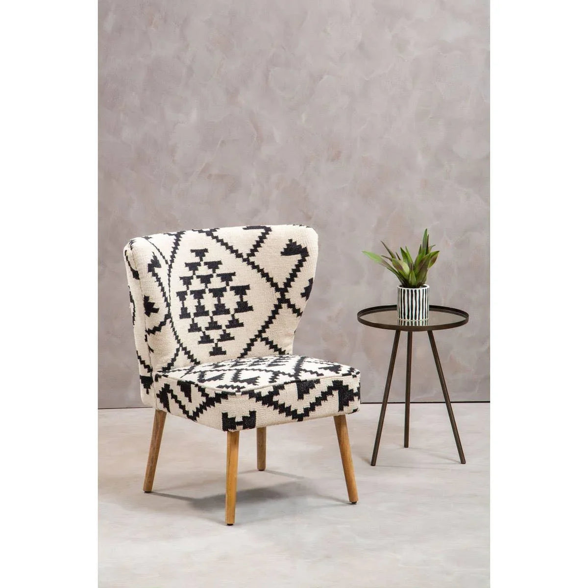 Patterned accent chair with wooden legs beside round side table and plant