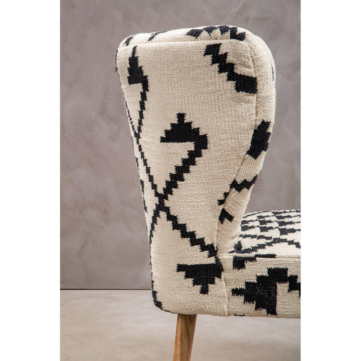 Accent chair with cream and black geometric upholstery and wooden legs, side angle view