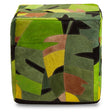 A square pouffe covered in a vibrant botanical print featuring various shades of green, yellow, and brown leaves. The pouffe has a soft leather texture and a structured shape, suitable for use as a footrest or additional seating