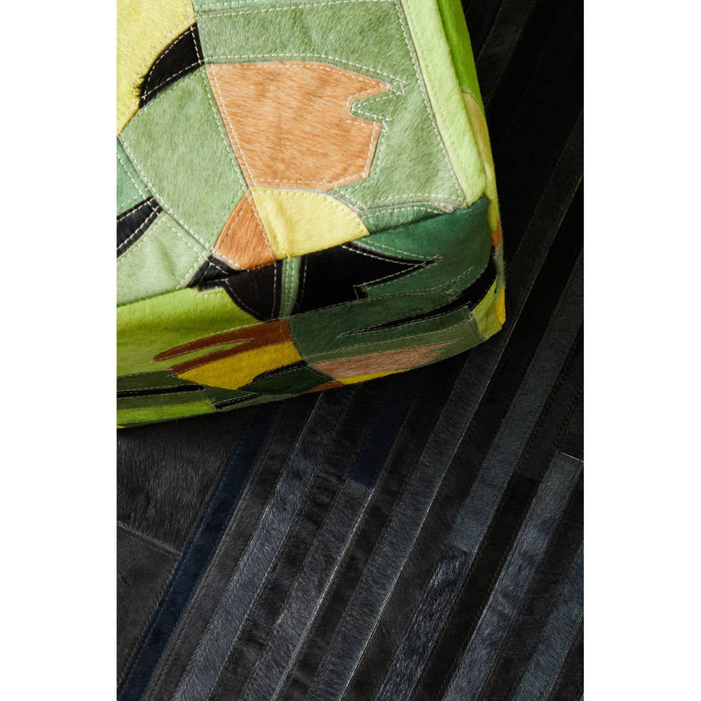 A close-up view of a colorful pouffe featuring a botanical leaf pattern in shades of green, orange, and yellow, resting on a textured black surface