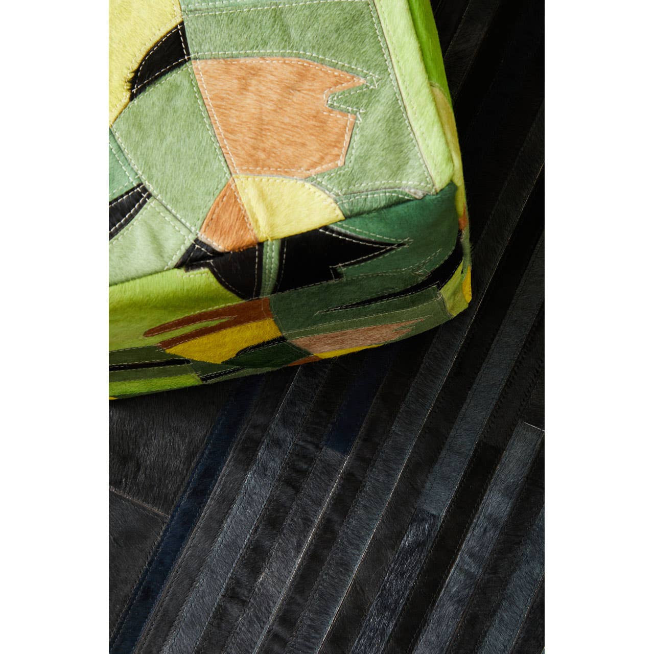 A close-up view of a colorful pouffe featuring a botanical leaf pattern in shades of green, orange, and yellow, resting on a textured black surface