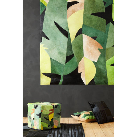 A colorful pouffe featuring a botanical design with various shades of green, yellow, and hints of pink, placed on a wooden floor. Behind it, a large wall art piece showcases abstract leaf patterns in similar colors, creating a vibrant and cohesive decor theme