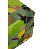 A close-up view of a corner of the Safira Botanical Leather Pouffe, featuring a vibrant, multicolored design with green, yellow, and black botanical patterns on a textured leather surface. The pouffe has a cube shape with clean edges and a slightly padded appearance