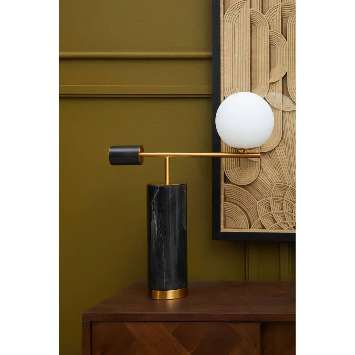Modern table lamp with black marble base, gold frame and white globe shade on wooden unit
