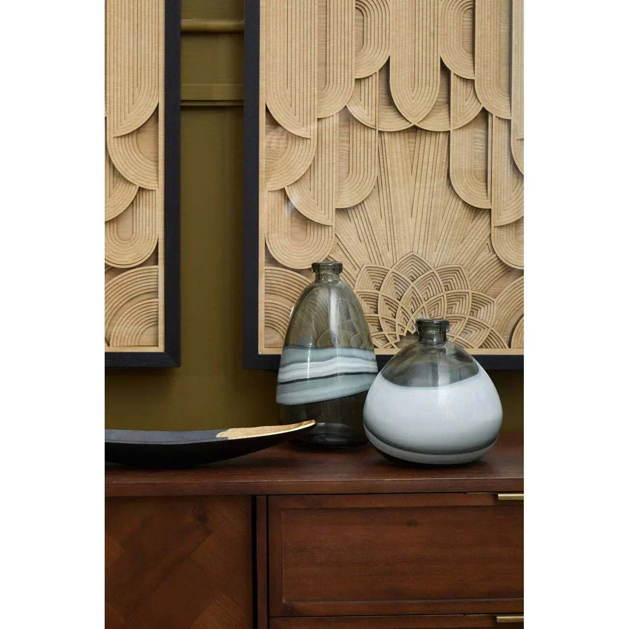 Two glass vases with grey and white swirls on a wooden sideboard, decorative wall art behind