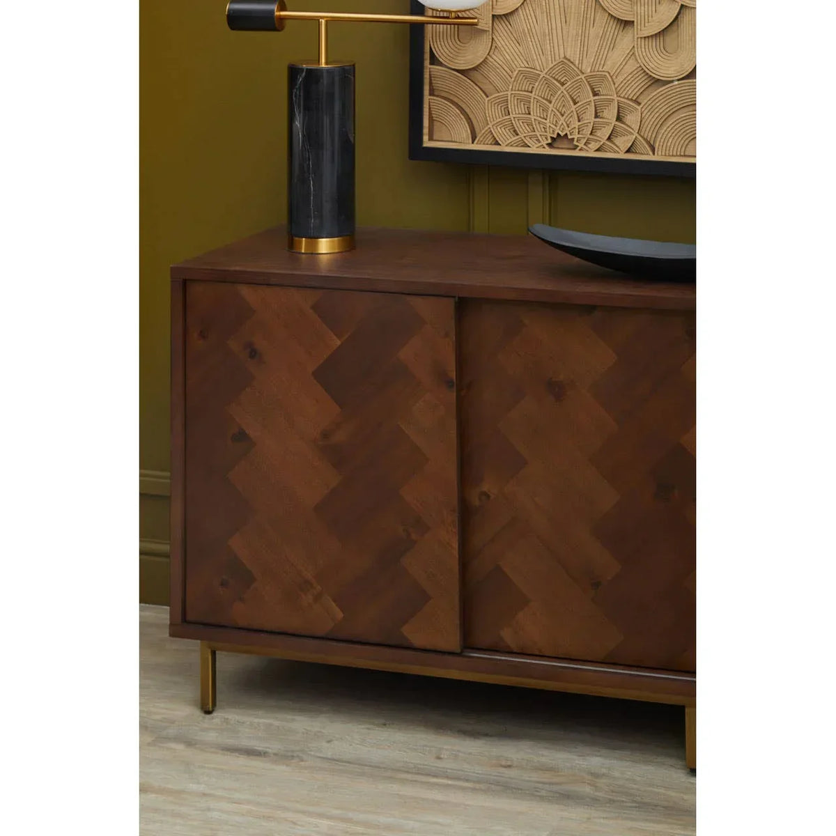 Walnut sideboard with herringbone wood doors and gold legs against green wall