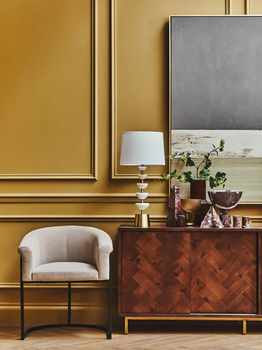 Velvet accent chair beside wooden sideboard with lamp, decor and abstract wall art