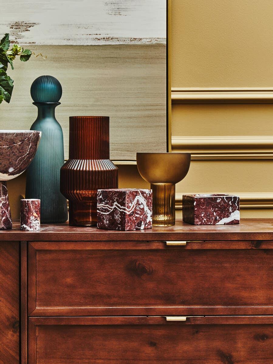 Wood sideboard with marble decor, ribbed glass vases and brass accent against beige wall