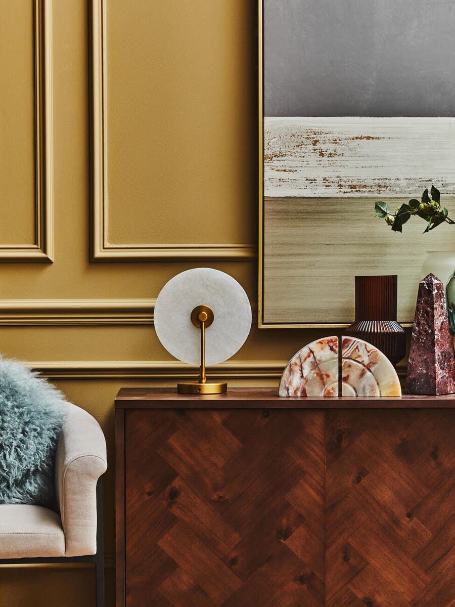Wood sideboard with modern decor accents and abstract art against gold panel wall