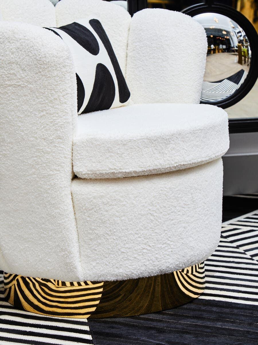 White boucle accent chair with black and gold swirl base, monochrome cushion on striped rug