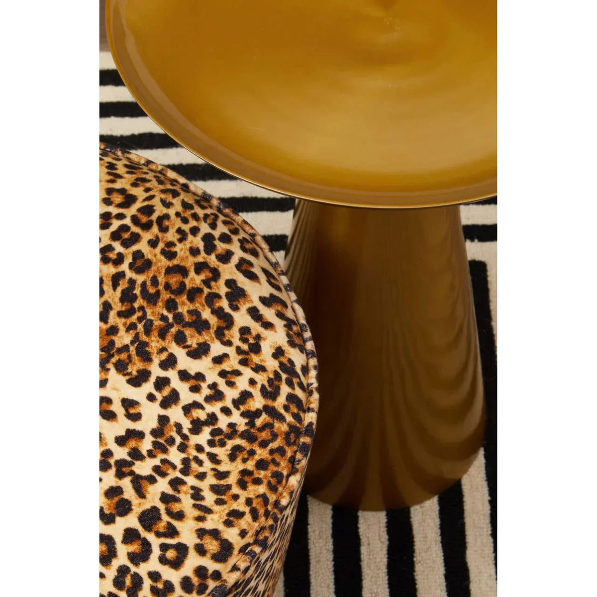 Leopard print ottoman beside gold metal side table on striped rug
