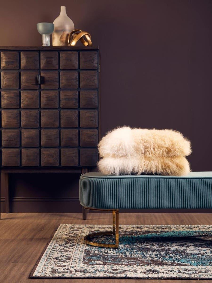 Velvet bench with gold metal legs and faux fur cushion beside dark wood cabinet on patterned rug