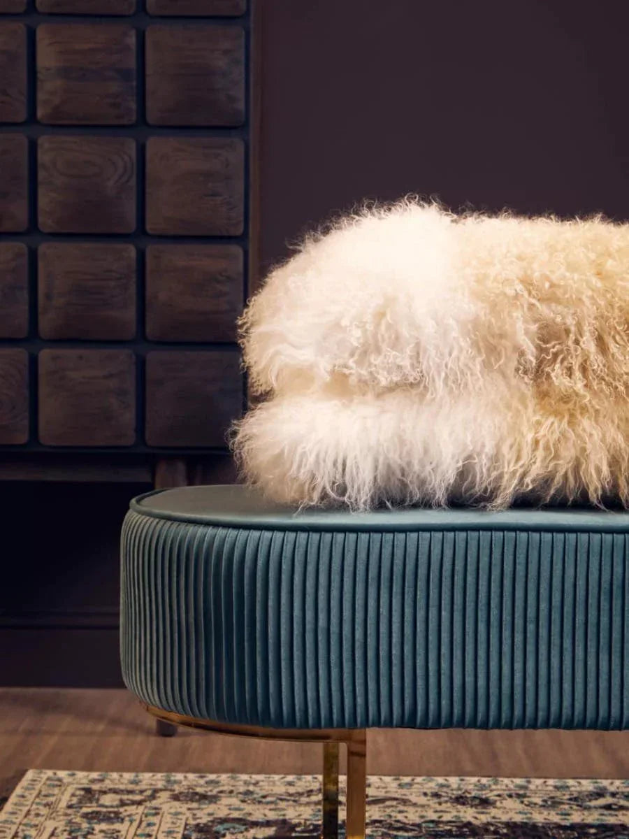Round teal velvet ottoman with gold legs, styled with cream sheepskin throw on patterned rug