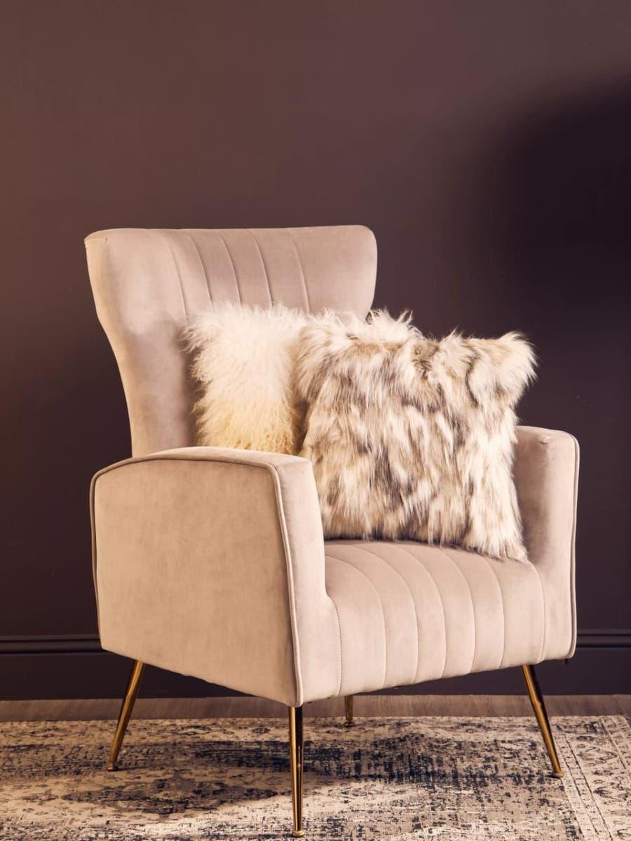 Beige accent chair with gold legs and faux fur cushions on patterned rug