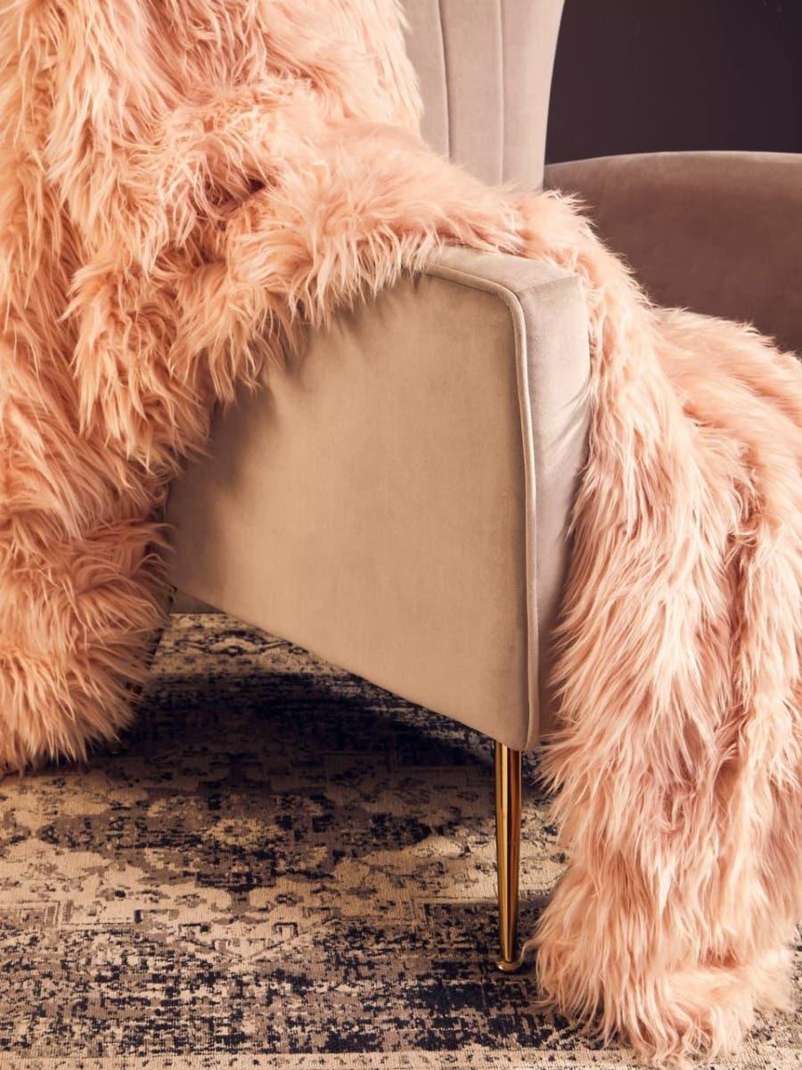 Beige velvet armchair with gold legs and pink faux fur throw on patterned rug