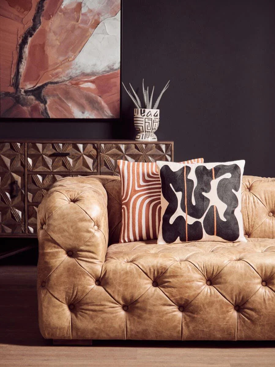 Tan leather sofa with tufted design, geometric cushions, and wooden sideboard in living room