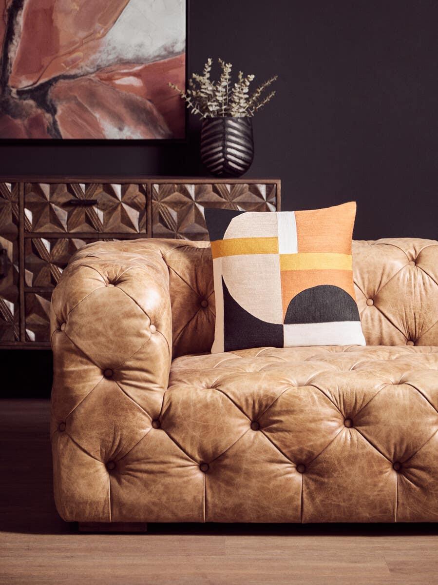 Tan leather sofa with button tufting and geometric cushion in modern living room