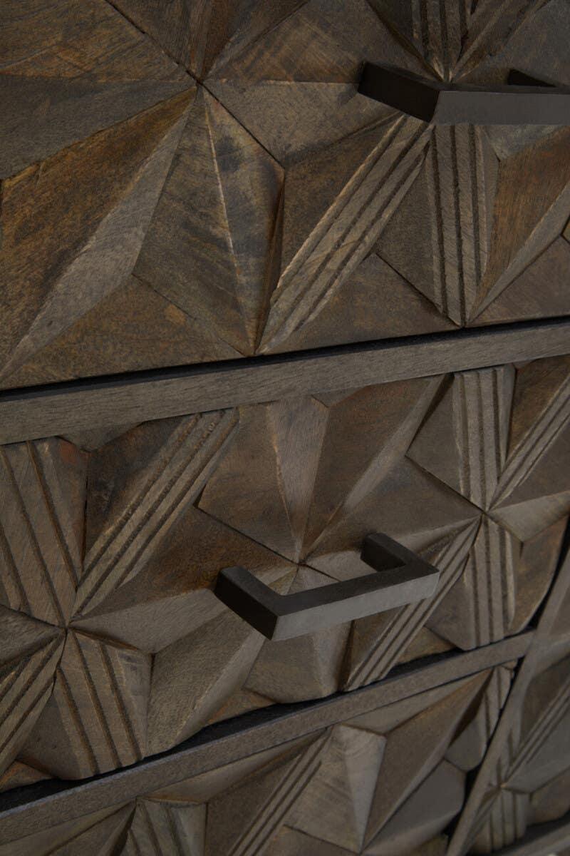 Geometric carved wood drawer fronts with black metal handles on a chest of drawers