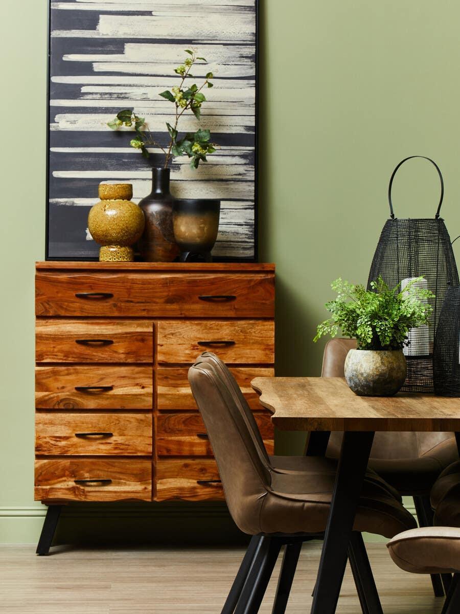 Wood chest of drawers with modern decor beside oak dining table and brown chairs