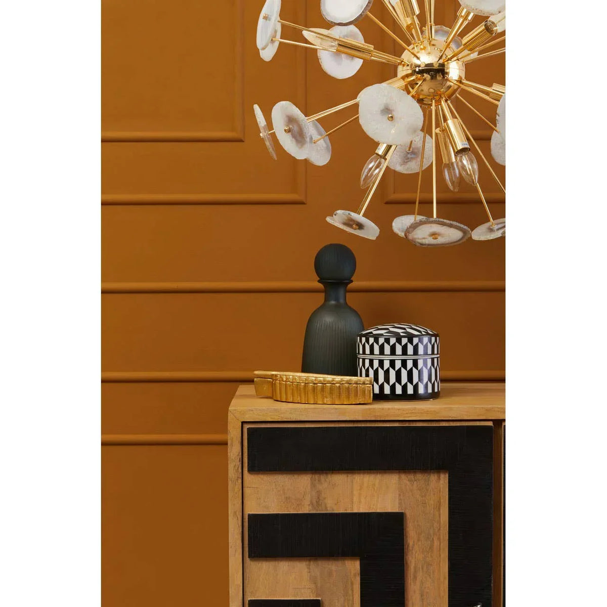 Wooden sideboard with black geometric detail and gold chandelier against ochre wall