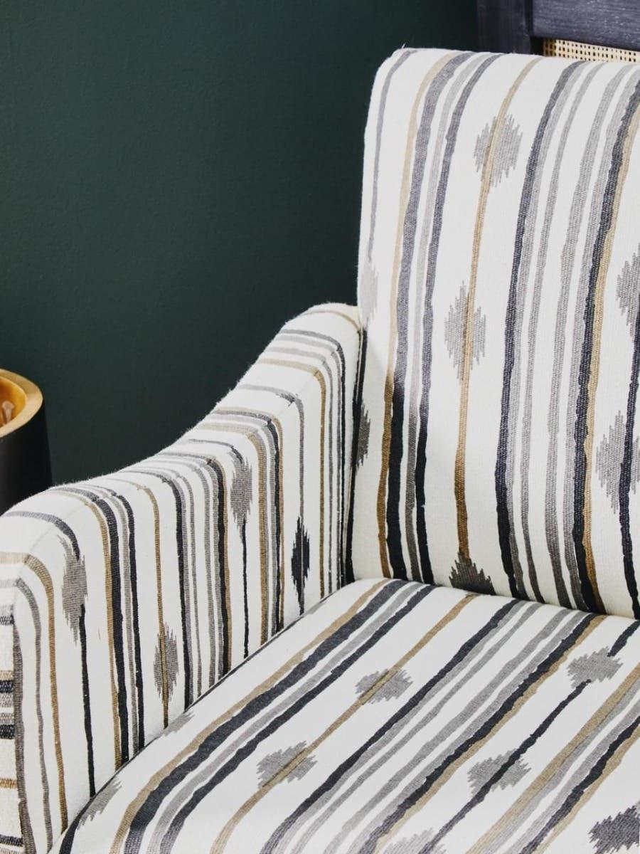 Striped fabric armchair with beige, grey, and black pattern against dark green wall