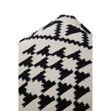 Square pouffe featuring a bold black and white geometric pattern with zigzag and triangular designs, showcasing a textured fabric surface. The pouffe has a slightly tapered top and is designed for versatile use in home decor