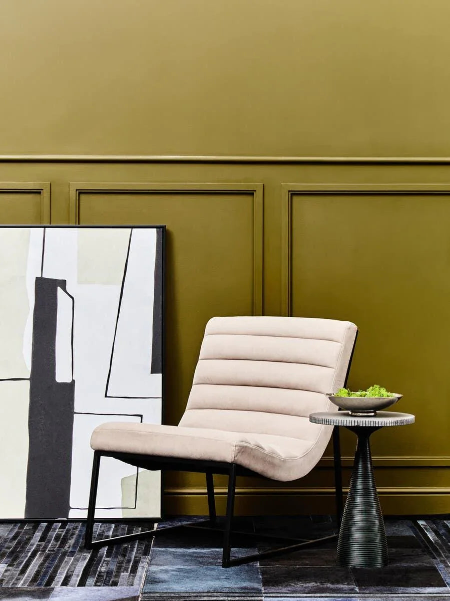 Modern beige accent chair with black metal legs beside side table and abstract artwork