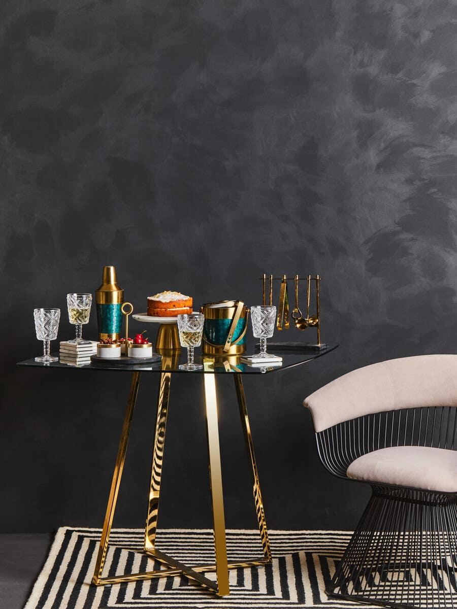 Glass and gold dining table with barware and cake, modern chair on striped rug