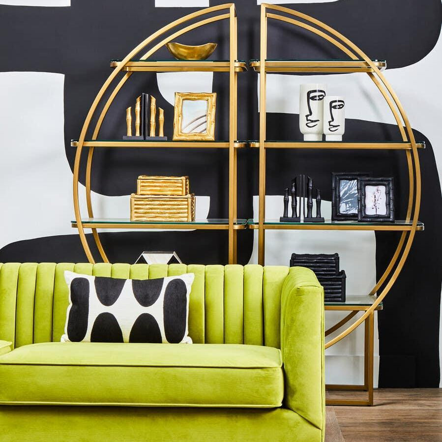 Green velvet sofa with black and white cushion, gold frame shelving unit, modern decor