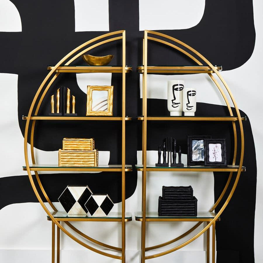 Gold metal and glass circular shelving unit with decorative ornaments and geometric boxes