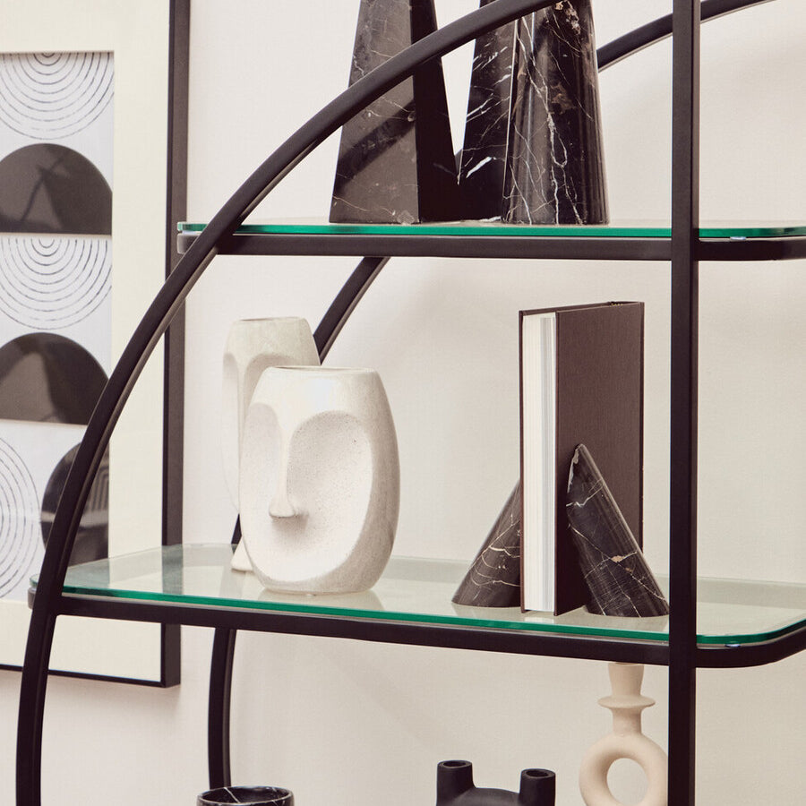 A black half-moon shelf unit featuring a sleek metal frame with multiple glass shelves. The shelves display various decorative items, including abstract sculptures and vases, against a neutral wall backdrop