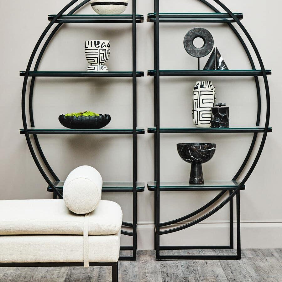 Modern black metal and glass shelving unit with decorative vases and a cream upholstered bench