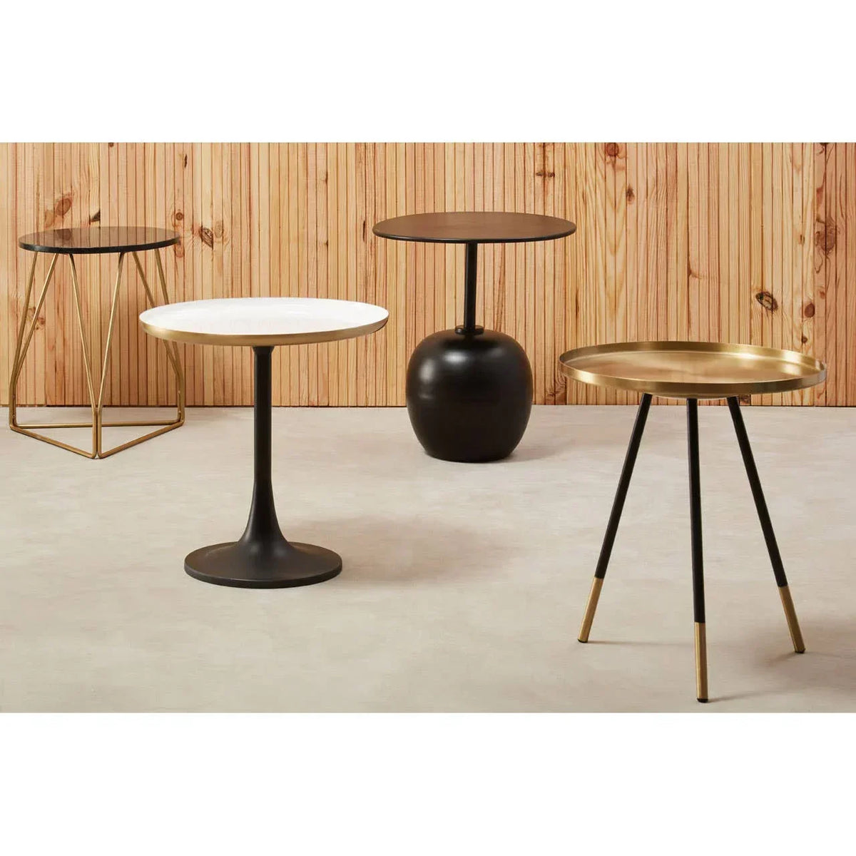 Modern accent tables in black, gold, and white finishes on neutral floor and wood panel wall