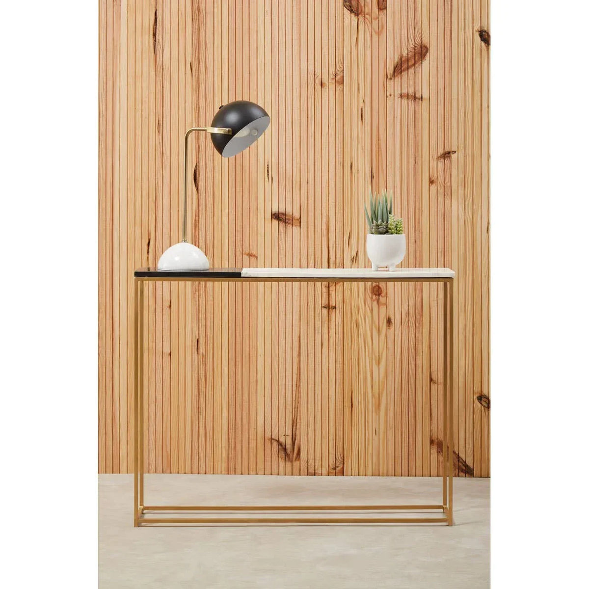 Modern console table with gold metal frame, white top, table lamp and potted plant