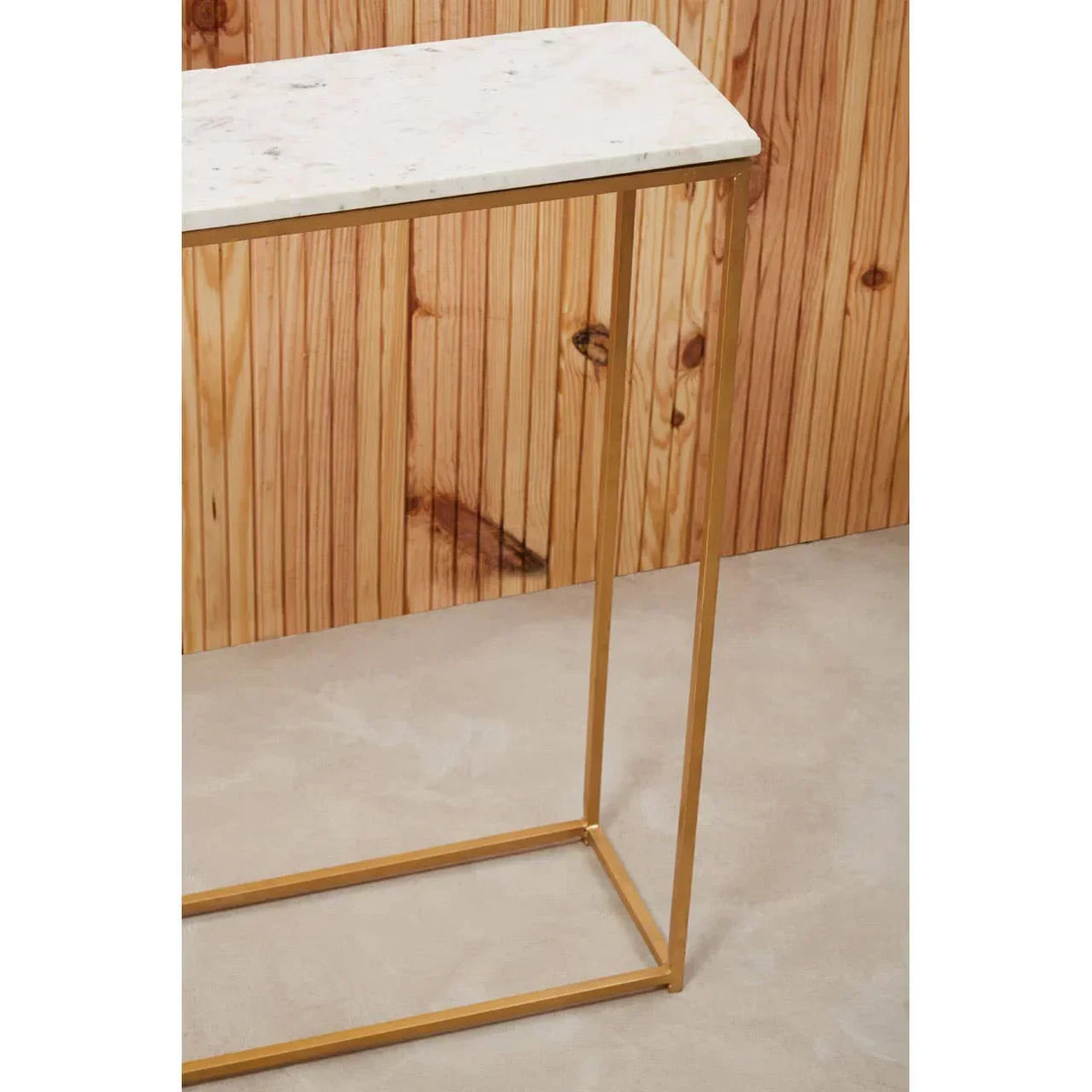 White marble console table with slim gold metal frame against wood panel wall