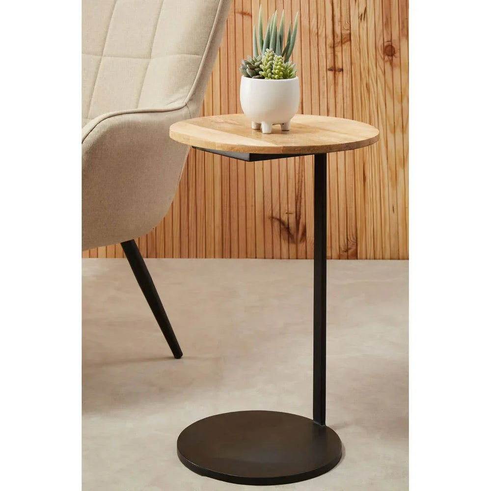 Round wooden side table with black metal base and succulent planter beside cream armchair