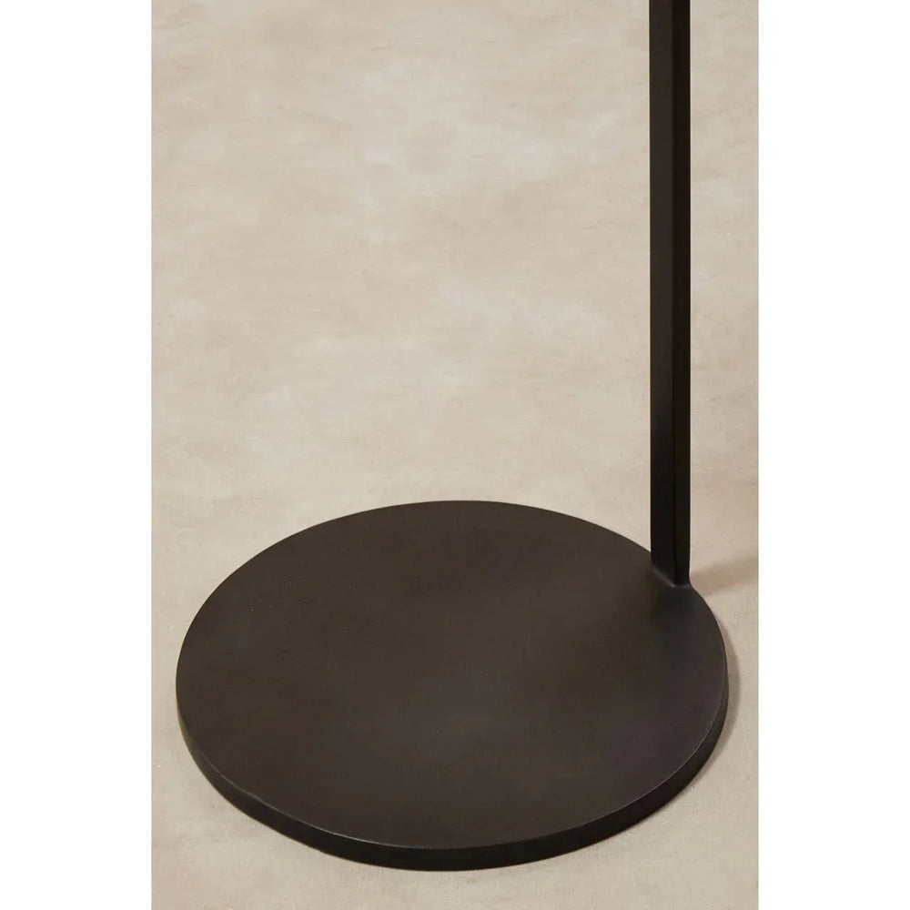 Black metal side table base on light beige floor, circular with minimalist design