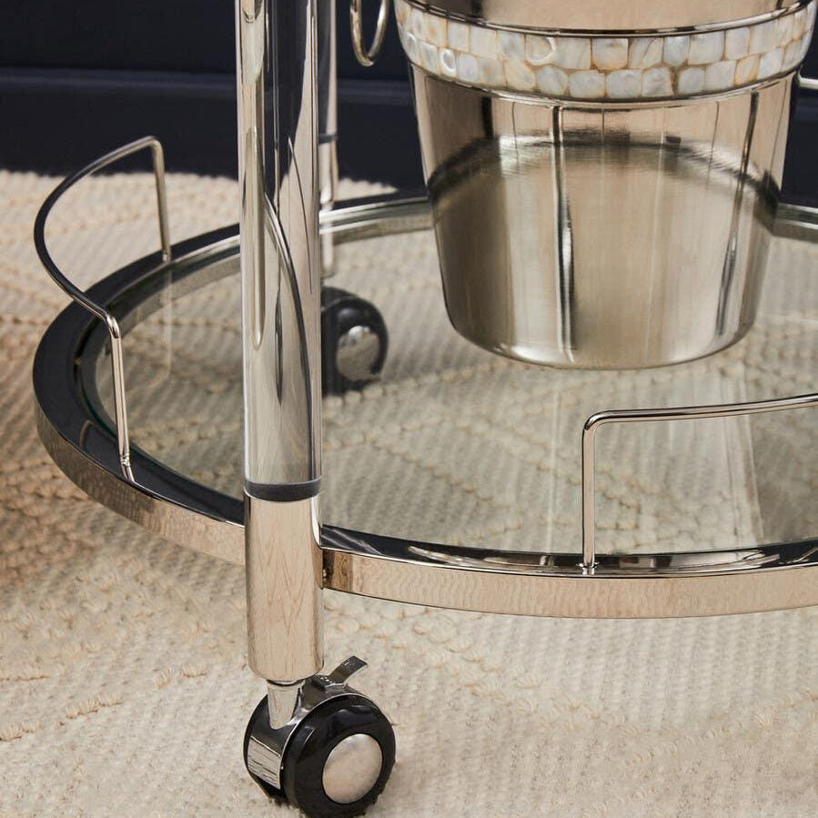 Chrome bar cart with glass shelf, metal ice bucket, and caster wheels on textured rug