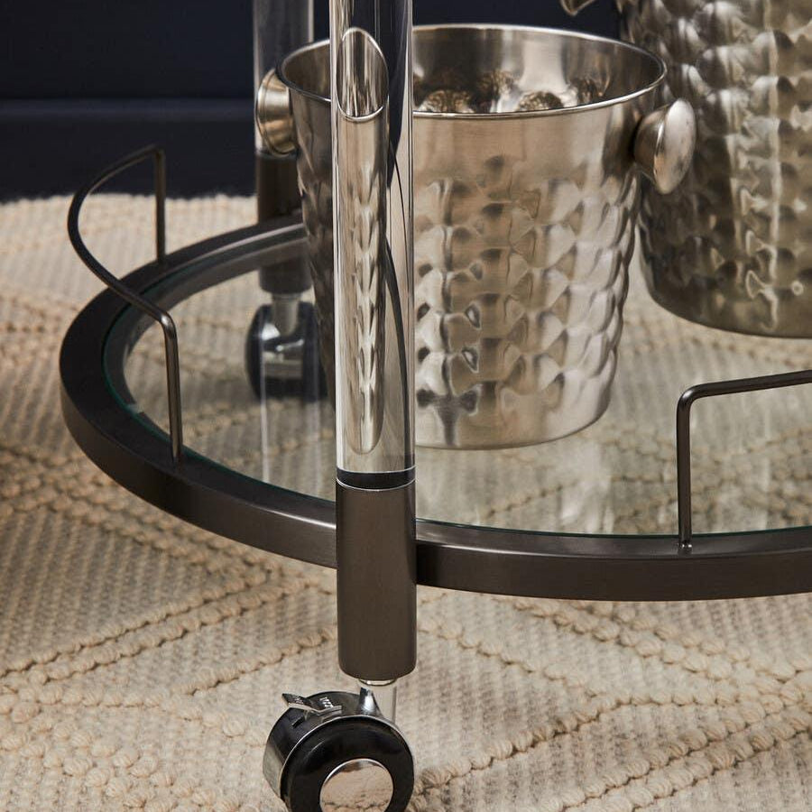 Glass and metal bar cart wheel closeup with chrome ice bucket on textured beige rug