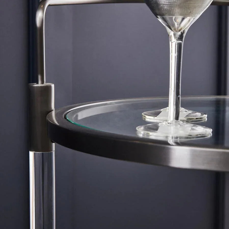 Modern glass and metal bar cart with a wine glass on top shelf, close-up view