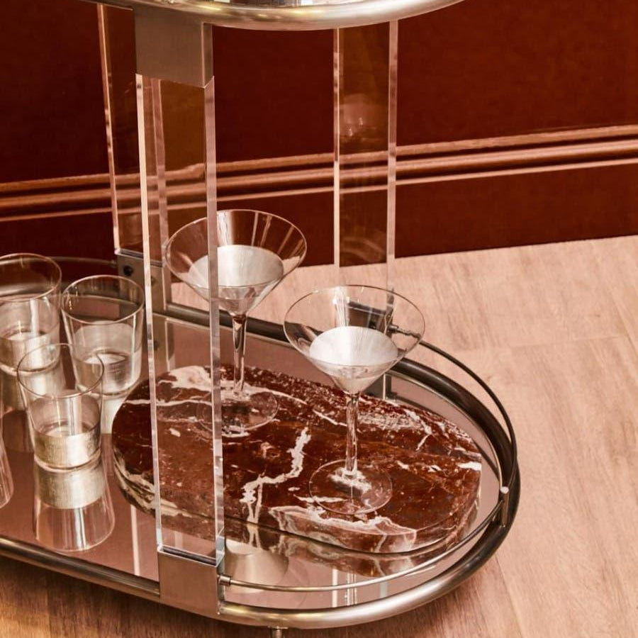 Modern drinks trolley with chrome frame, marble shelf, and glassware on wood floor