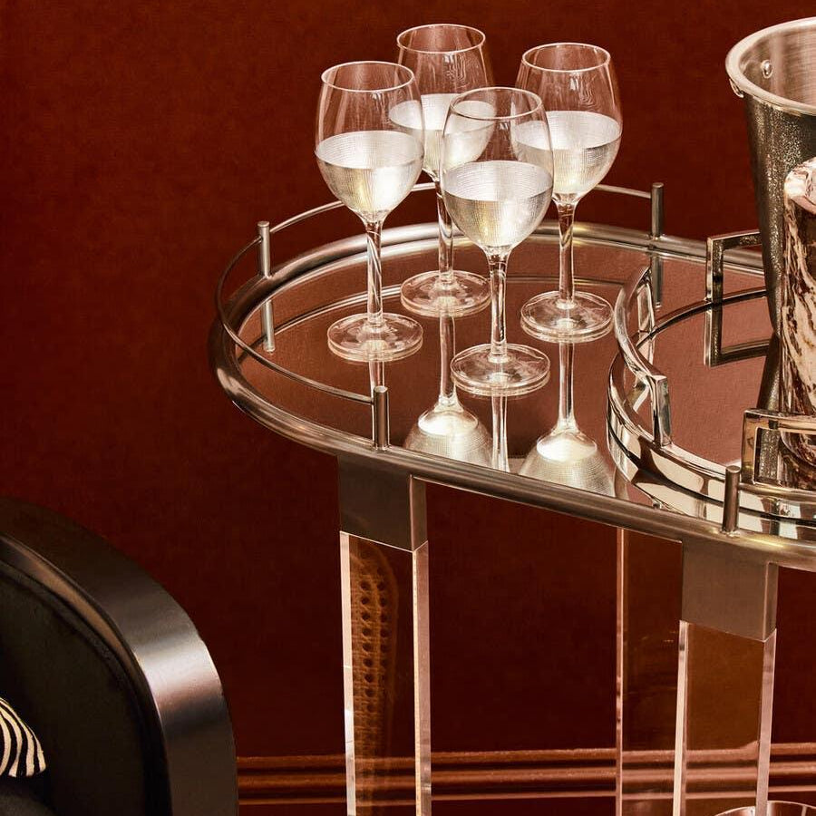 Glass drinks trolley with chrome trim, holding wine glasses and ice bucket against red wall
