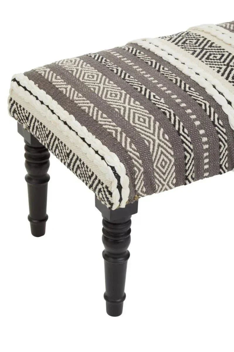Grey patterned upholstered bench with black turned wooden legs, close-up view