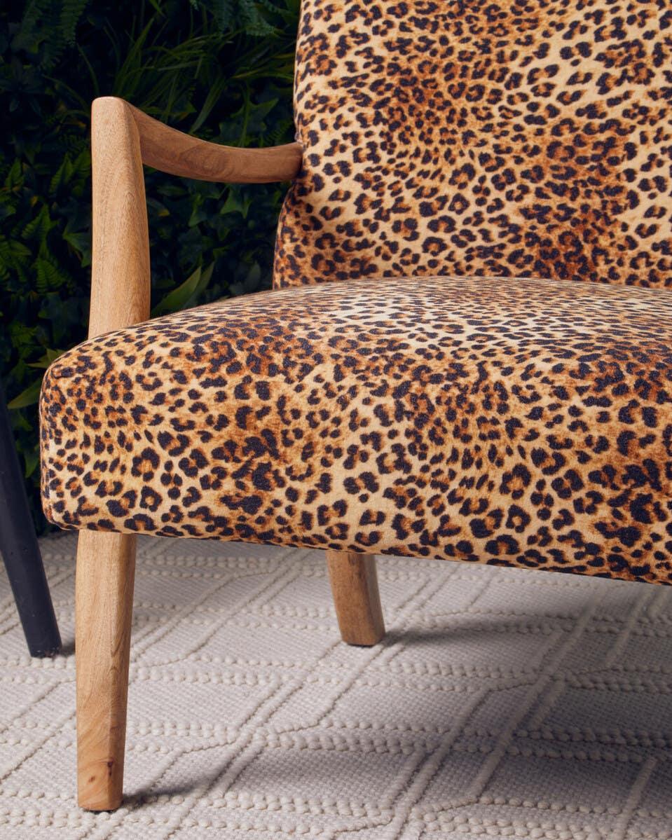 Leopard print accent chair with wooden armrest and tapered legs on textured rug
