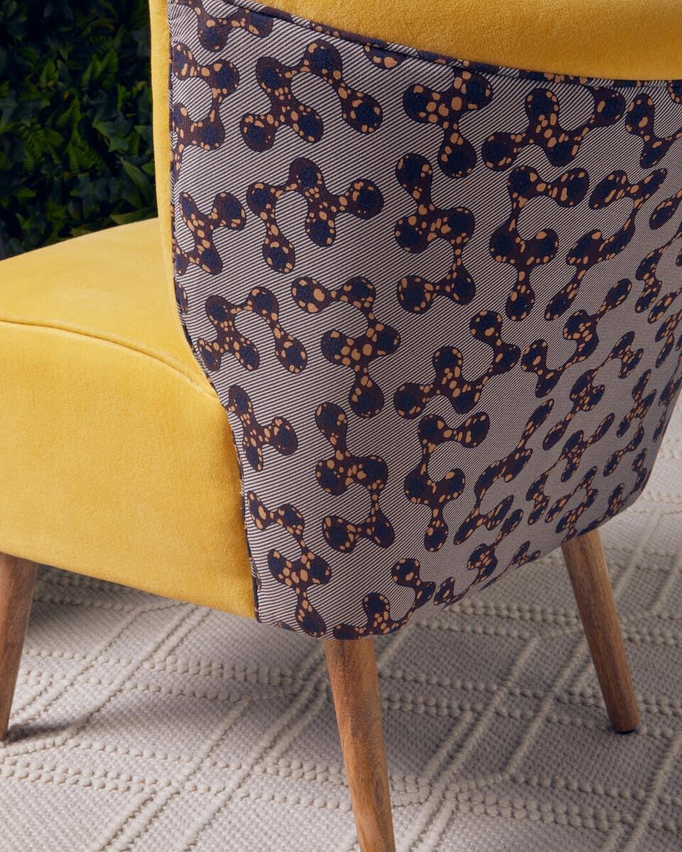 Yellow accent chair with patterned fabric back and wooden legs on textured rug