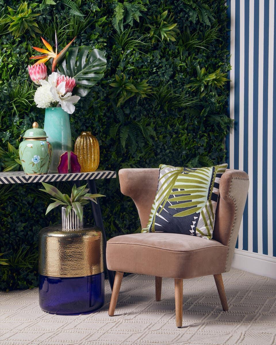 Velvet accent chair with leaf cushion beside gold glass side table and floral decor