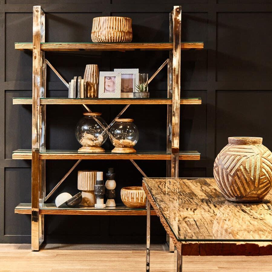 Glass and wood bookcase with decorative ornaments against black wall, marble dining table in front