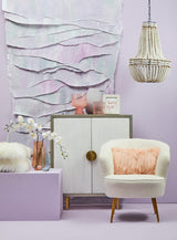 Cream and grey two-door cabinet made of mango wood, featuring a round gold handle, placed against a textured light purple wall. A white armchair with a pink cushion sits beside the cabinet, and a decorative pendant light hangs above. A small decorative vase and a bowl are positioned on top of the cabinet