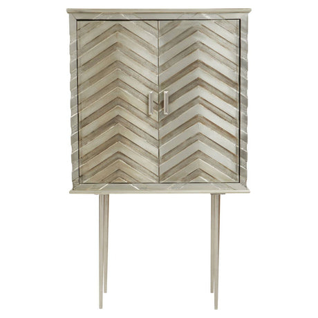 Two-door cabinet featuring a chevron pattern on the front, finished in a light color. The cabinet is elevated on slender legs and has a simple metal handle for opening the doors. The overall design is modern and stylish, suitable for home decor